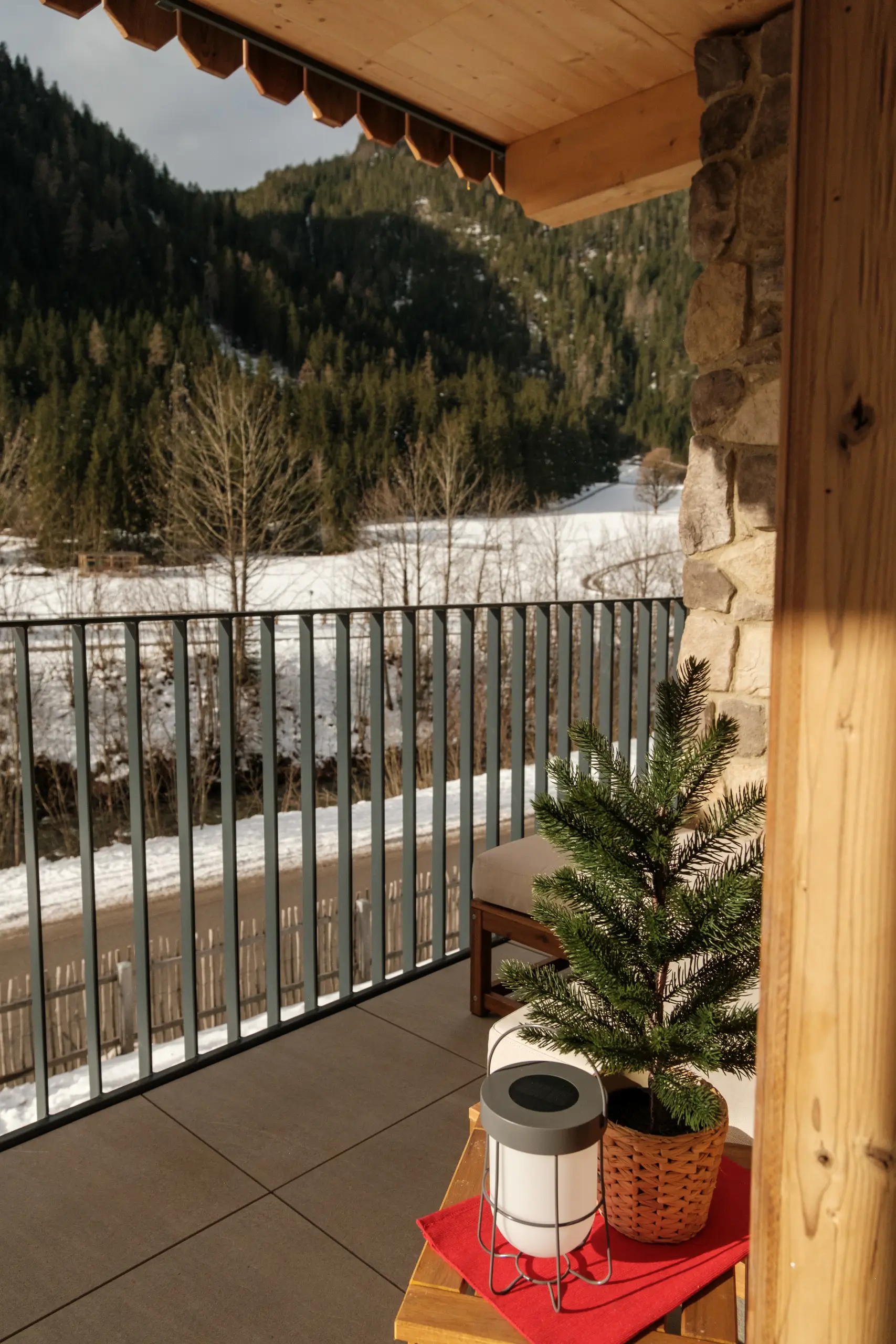 Balkonblick auf verschneite Berge mit kleinem Tannenbaum im Korb. Winterliche Alpenlandschaft.