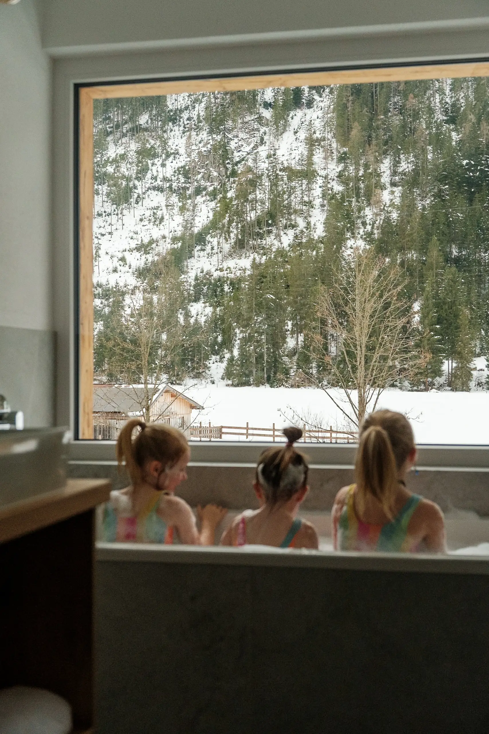 Drei Mädchen baden mit Blick auf verschneite Berge.