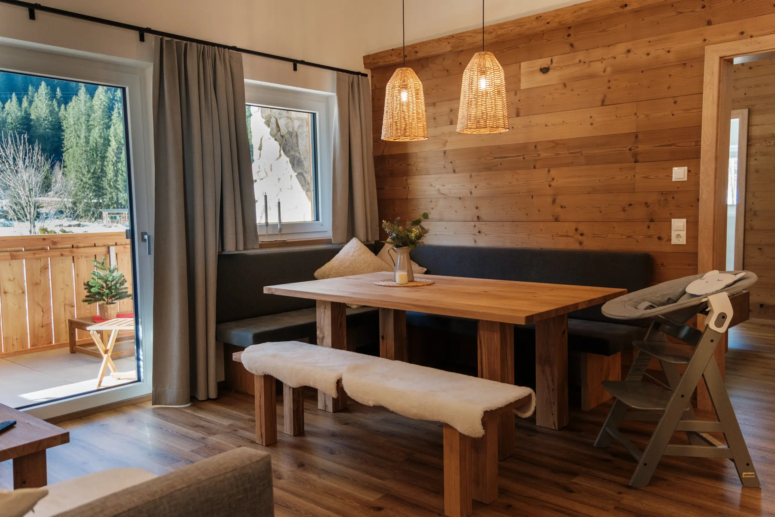 Gemütliches Esszimmer im Chalet-Stil mit Holzwand, Esstisch, Bank mit Fell und Blick auf die Berge.