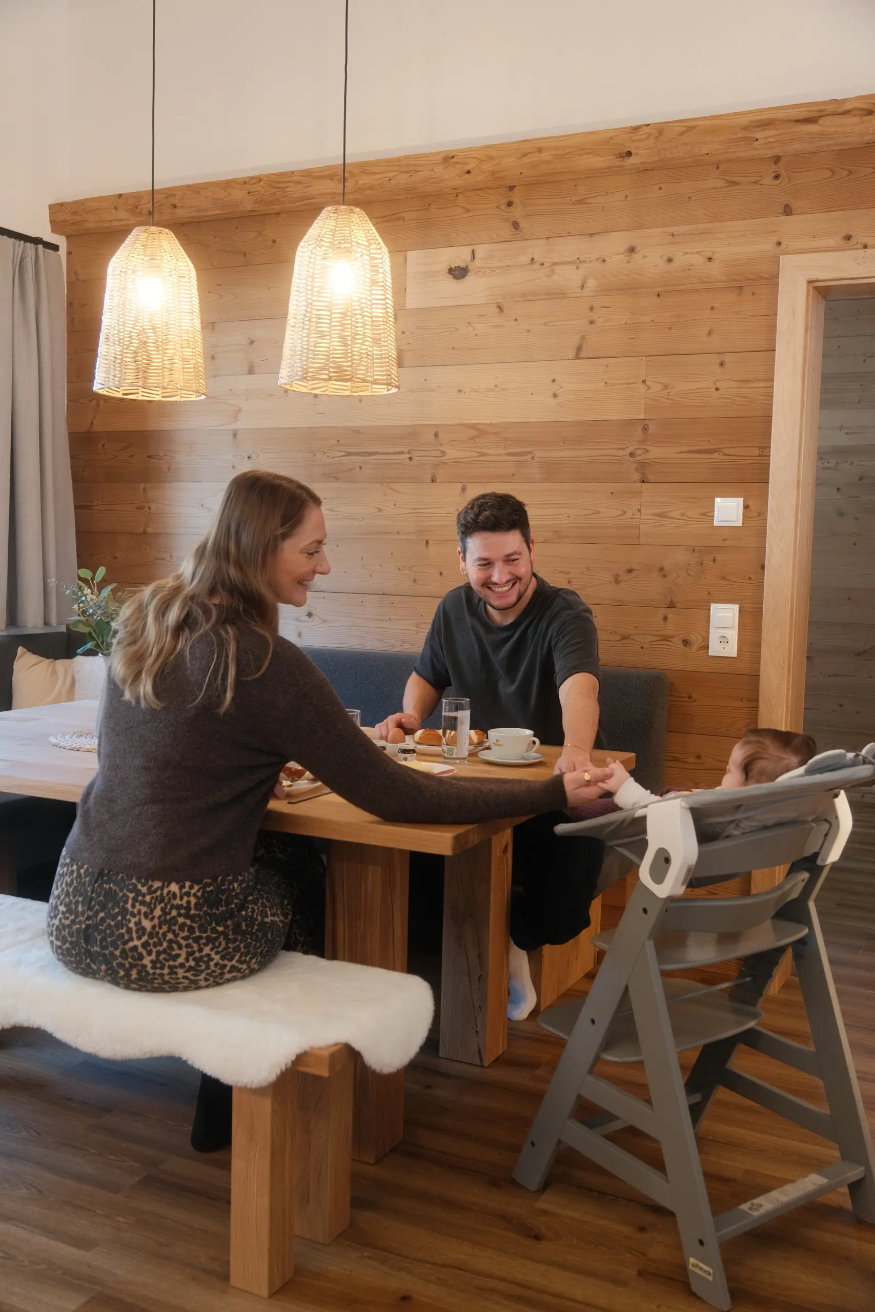 Familie am Holztisch mit Baby im Hochstuhl. Gemütliches Frühstück im Alpenstil.
