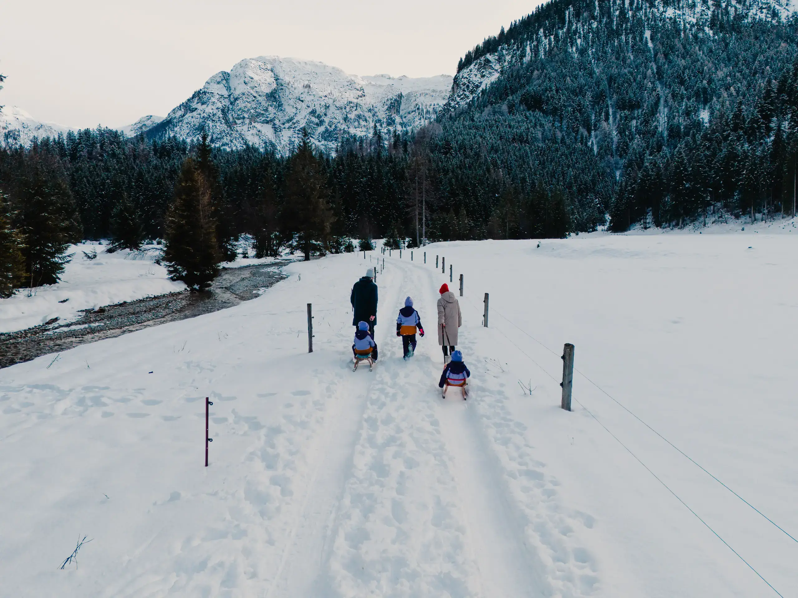 Familie mit Schlitten im Schnee vor Bergkulisse. Winterlandschaft in den Alpen.