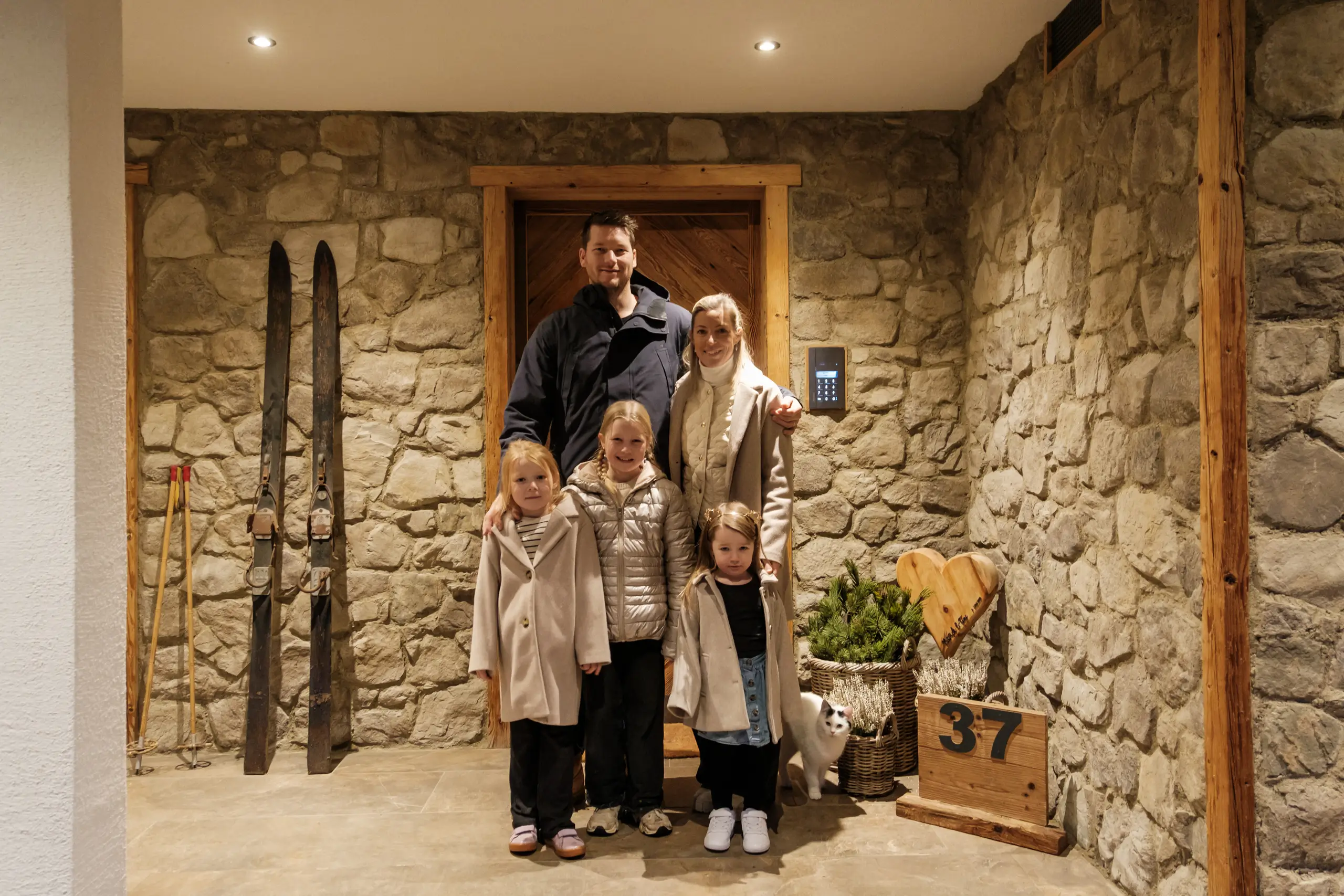 Familienfoto vor rustikaler Steinwand mit alten Skiern.