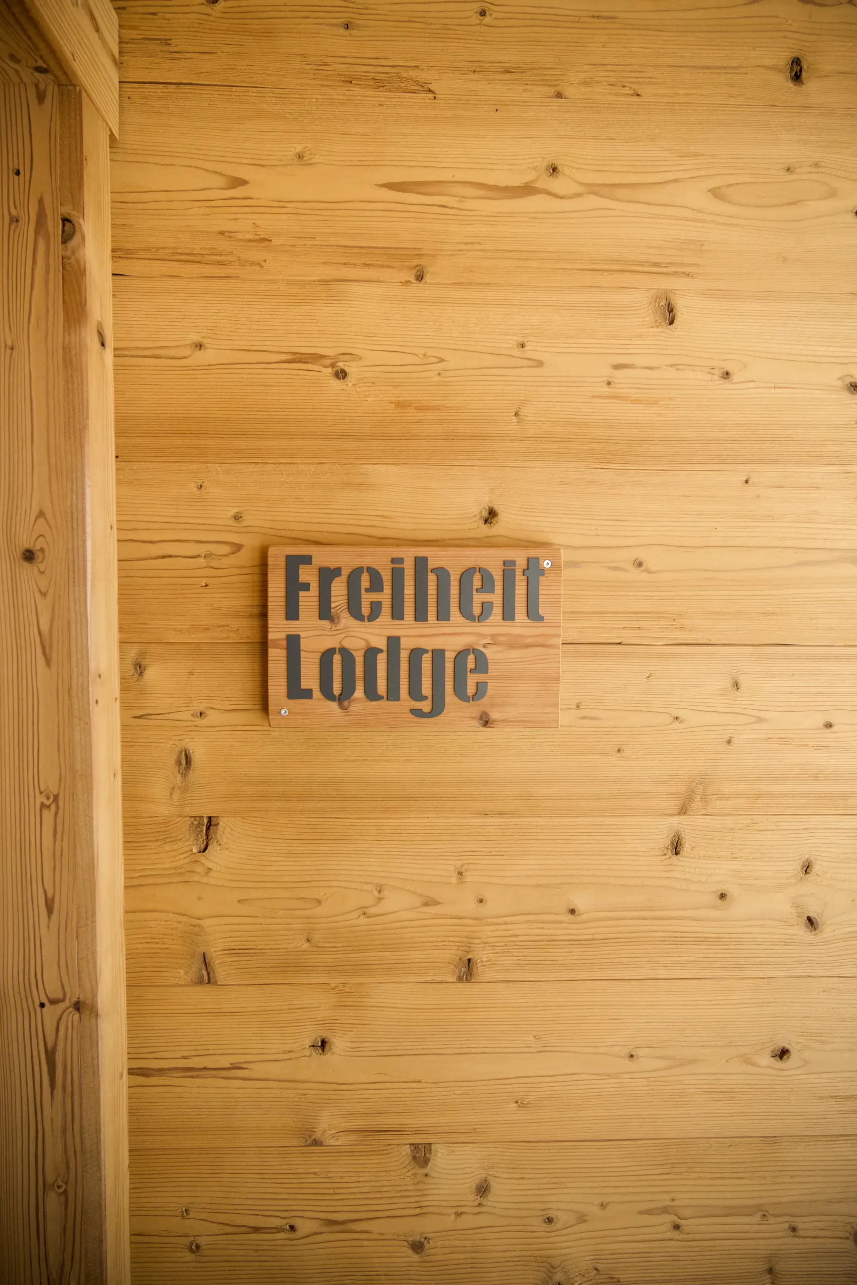 Holzschild mit der Aufschrift "Freiheit Lodge" an einer Holzwand.