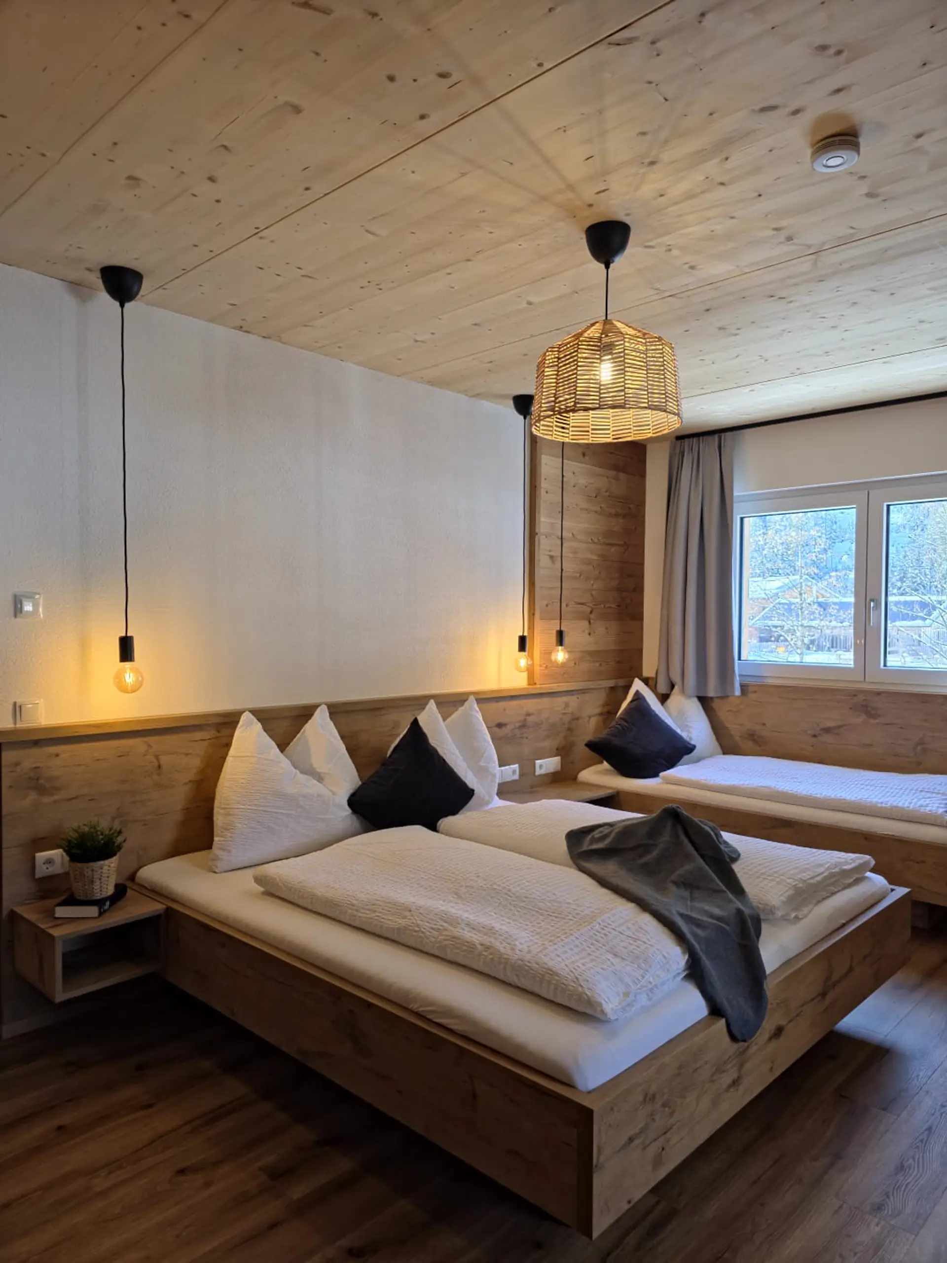 Gemütliches Schlafzimmer mit Holzbett, Nachttisch und Fenster. Helle, moderne Einrichtung im Alpenstil.