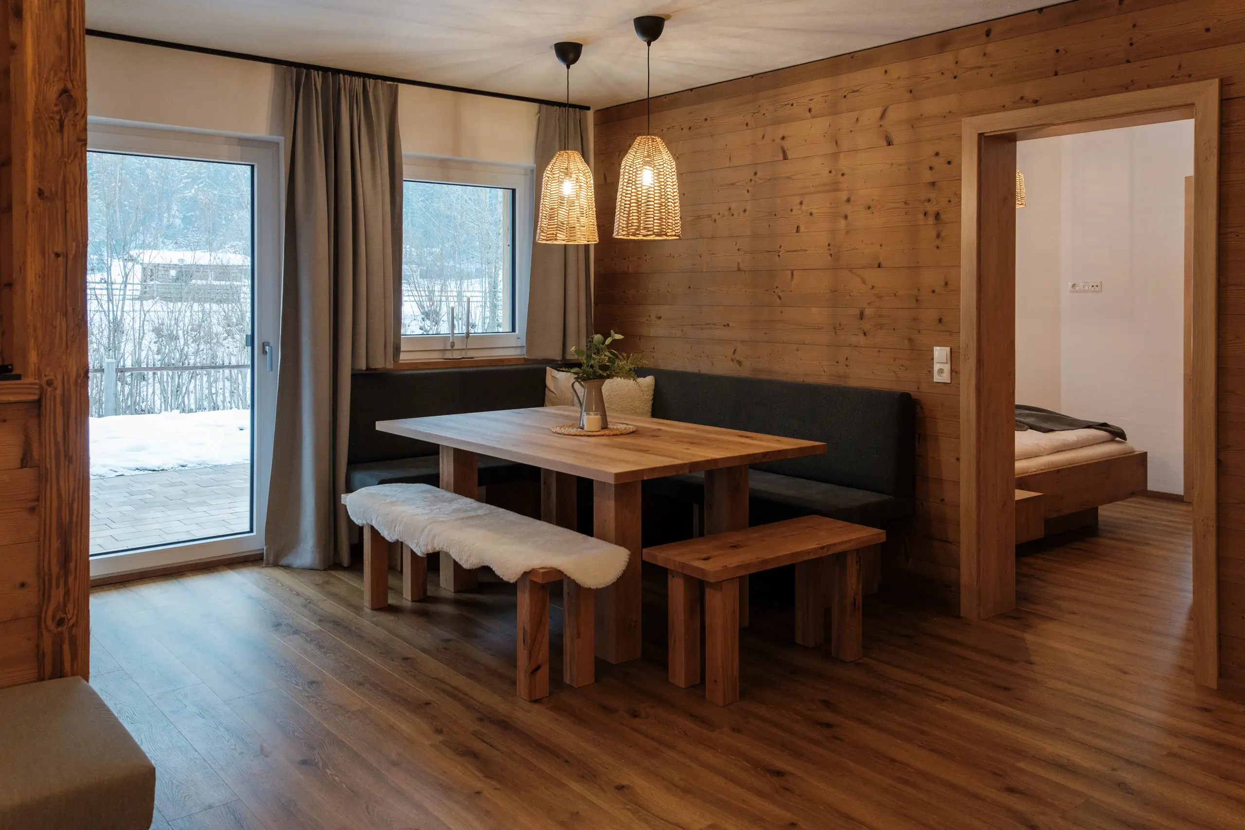 Gemütliche Essecke im Chalet-Stil mit Holztisch, Bank und Blick auf verschneite Landschaft