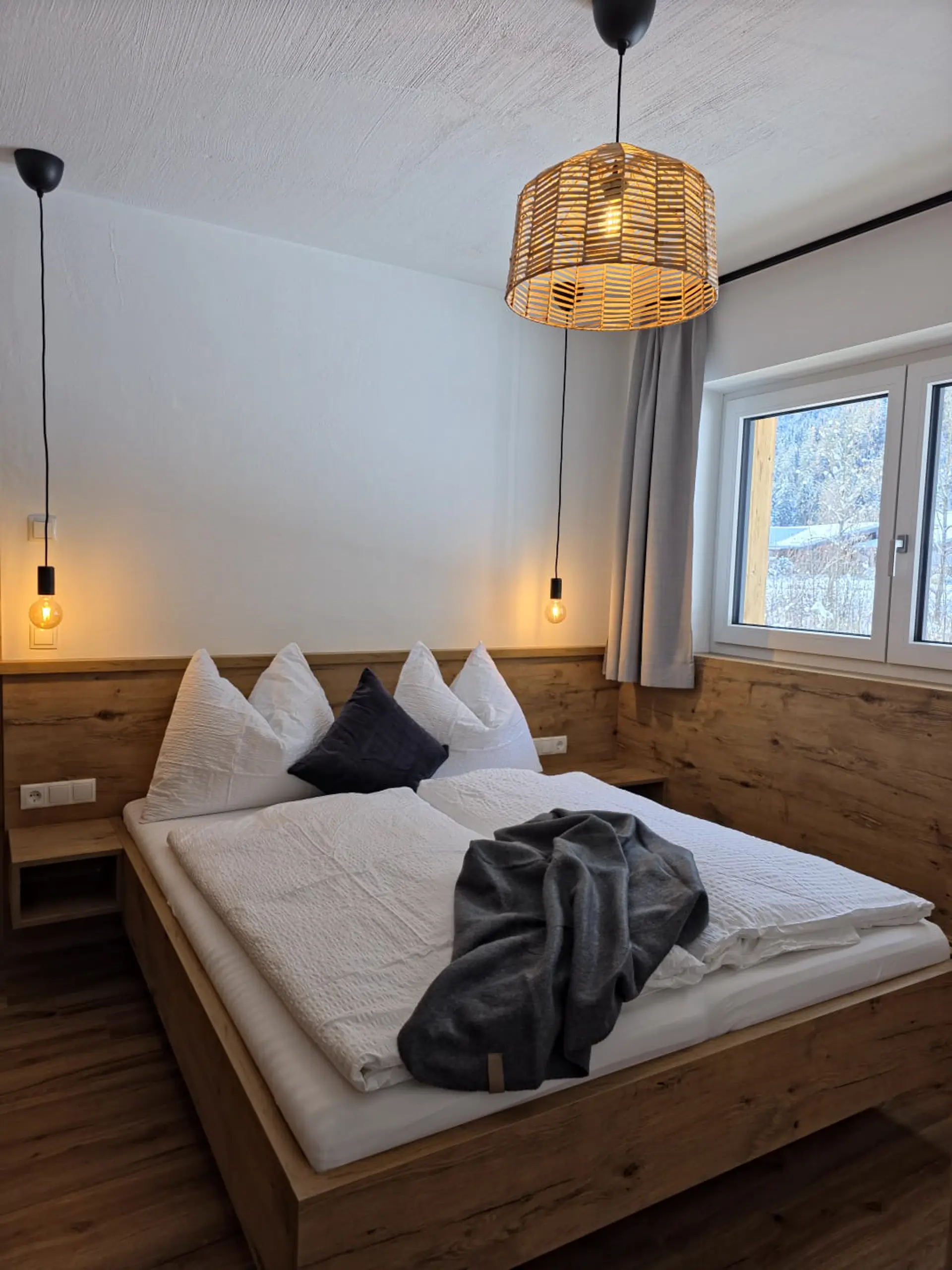 Gemütliches Schlafzimmer mit Holzbett, weißen Kissen und moderner Beleuchtung.