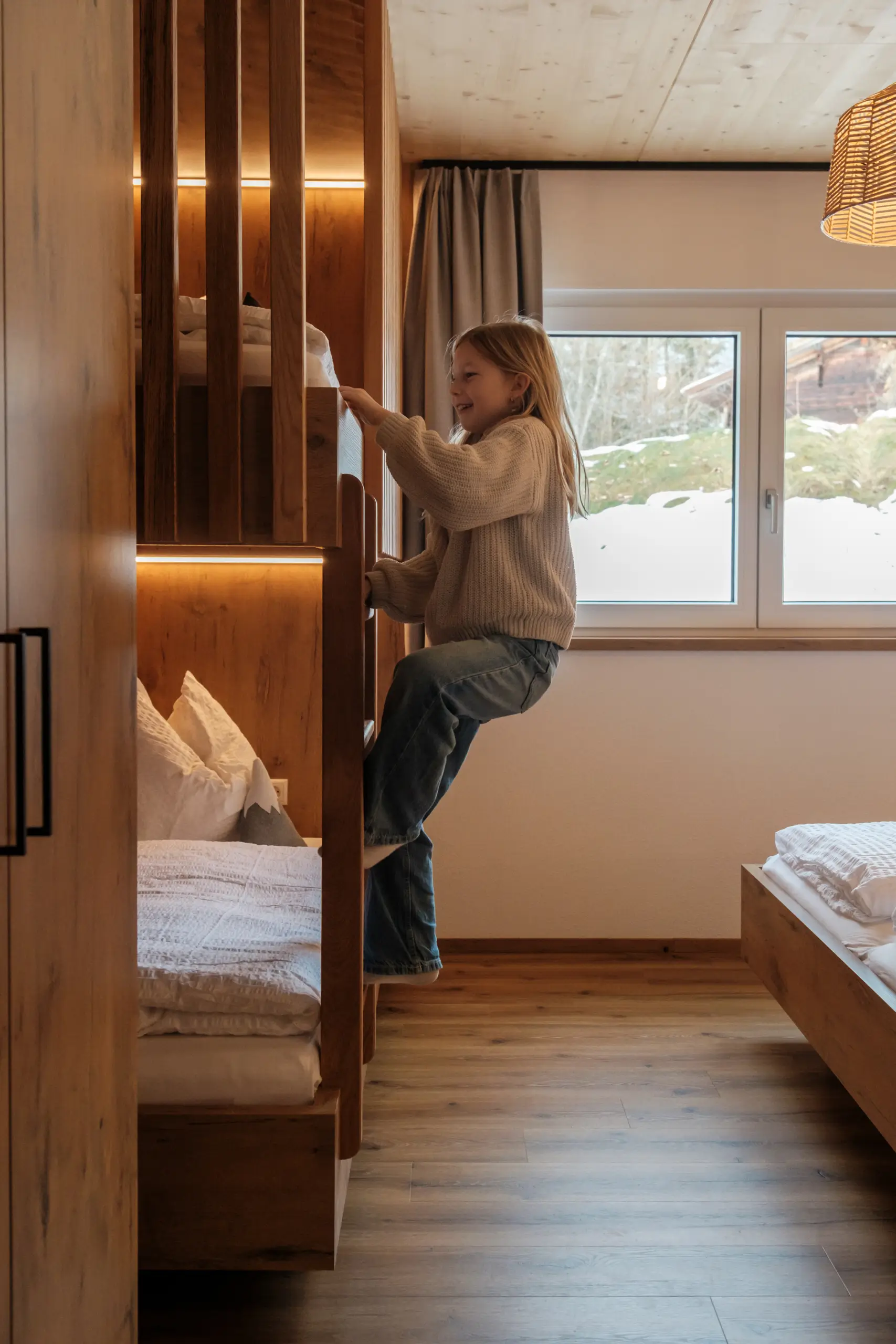 Fröhliches Mädchen klettert auf ein Holzbett im gemütlichen Zimmer.