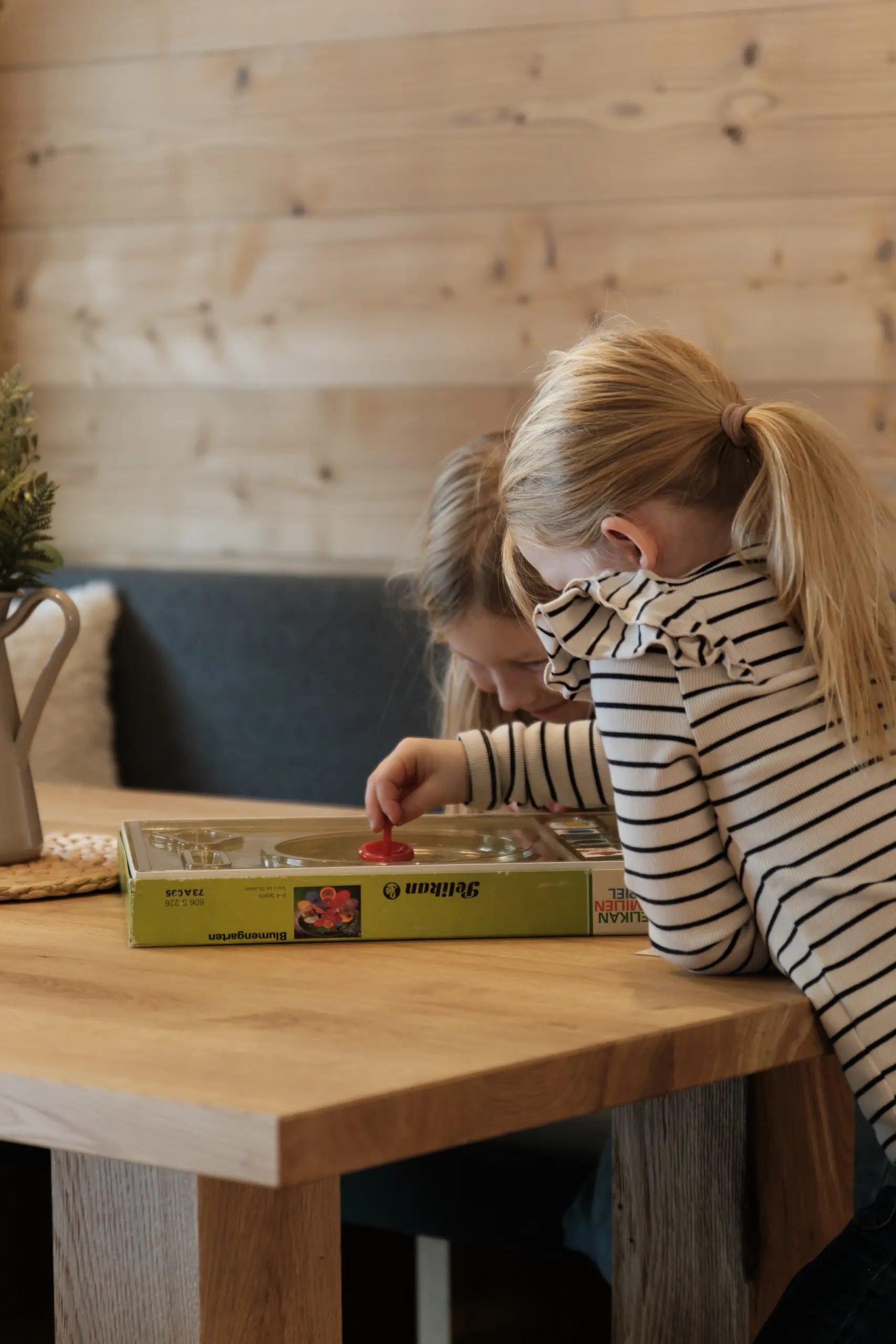 Blondes Mädchen spielt "Blumengarten" von Pelikan am Holztisch. Brettspiel für Kinder.
