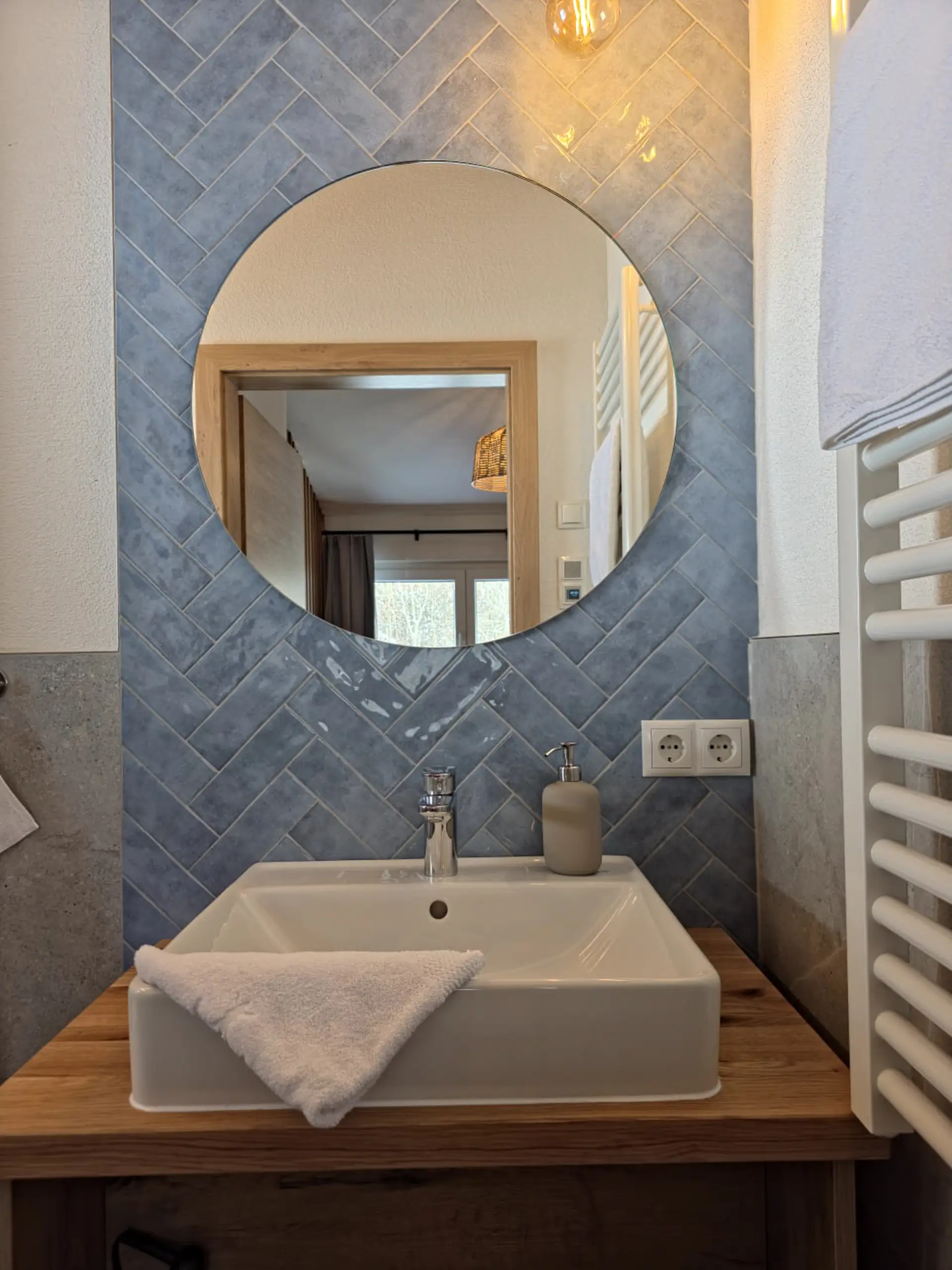 Modernes Badezimmer mit Waschbecken, Spiegel und blauen Fliesen. Helle, einladende Atmosphäre.