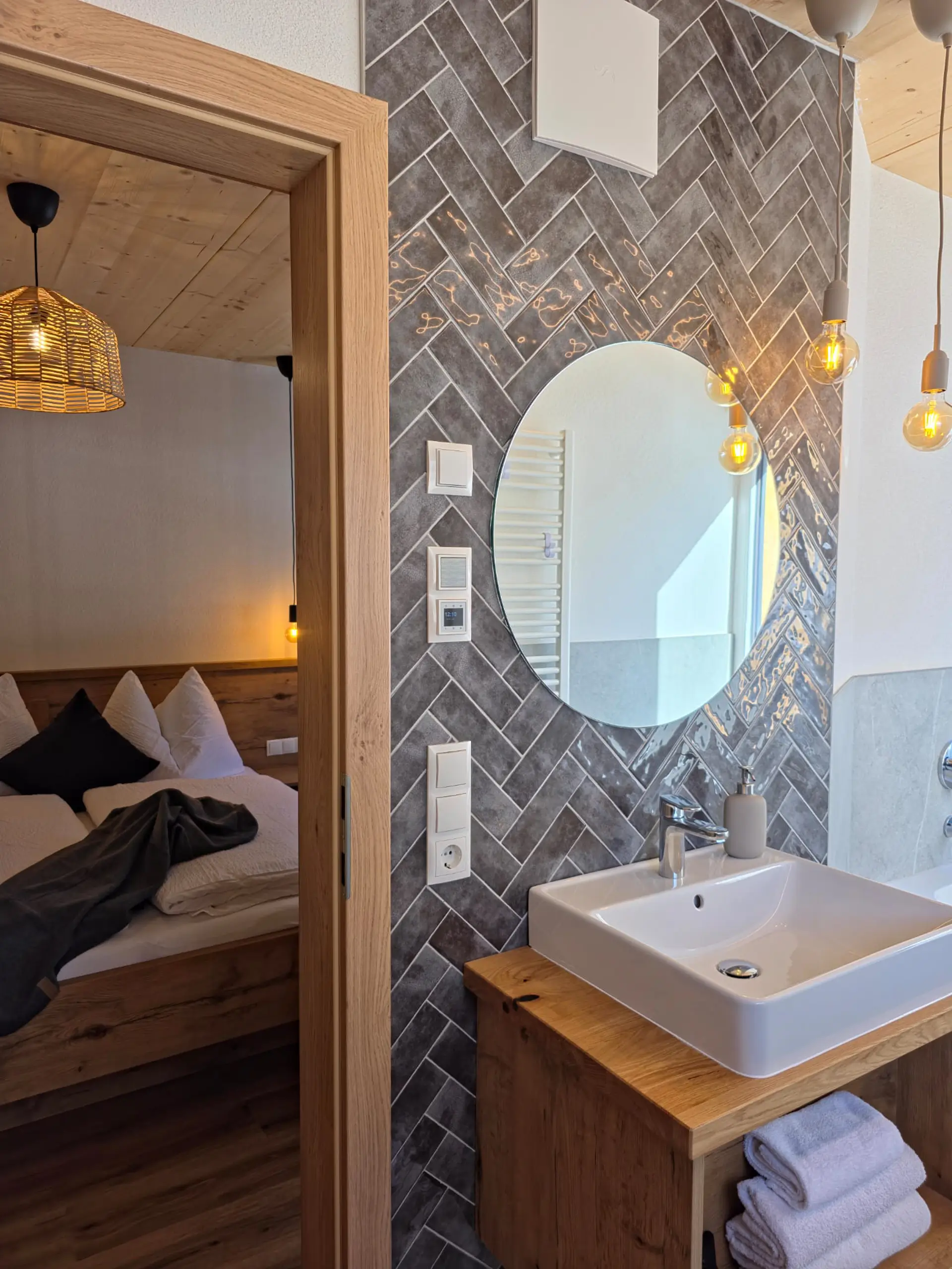 Modernes Badezimmer mit Waschbecken, Spiegel und Blick ins Schlafzimmer.