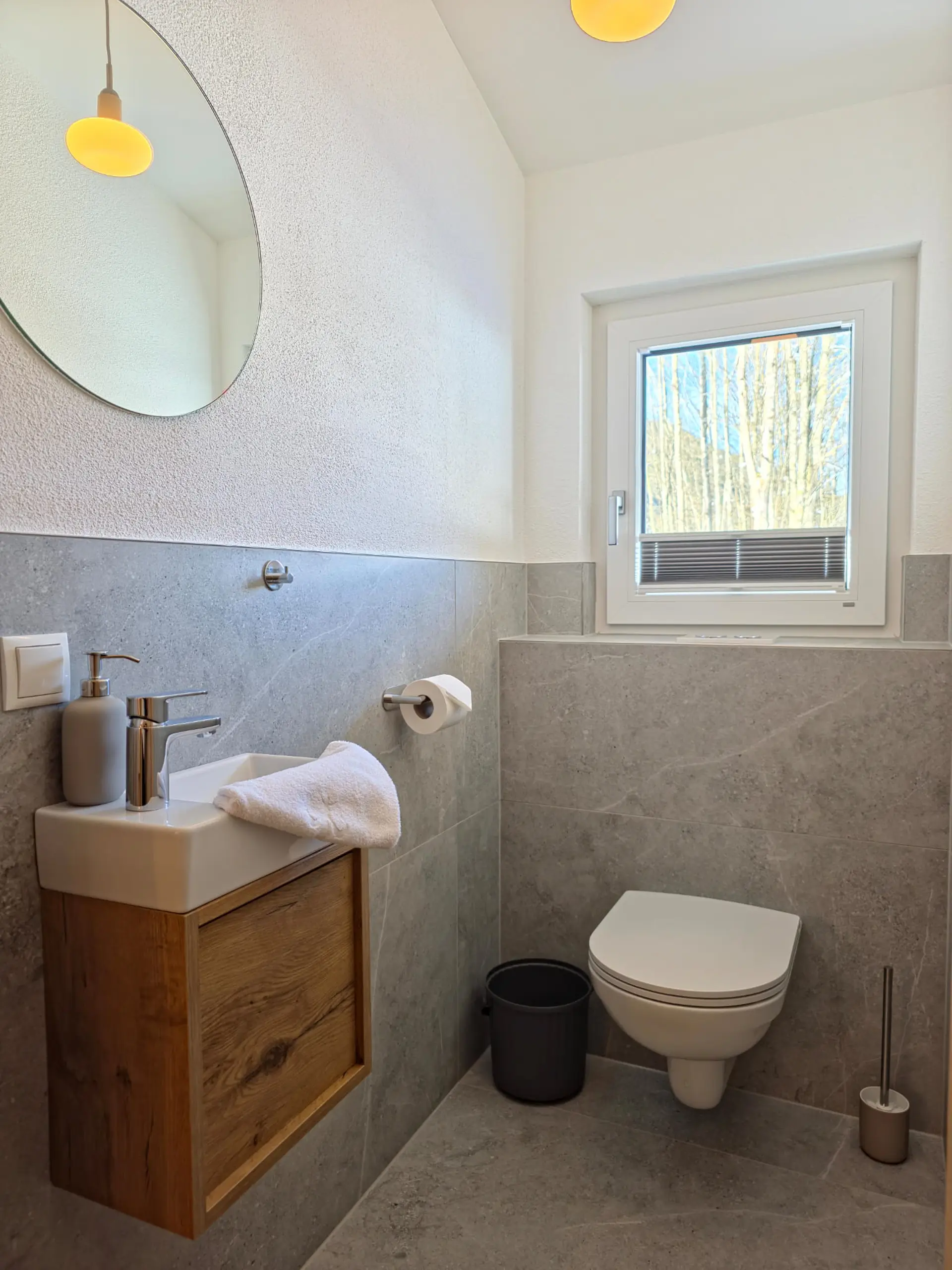 Modernes graues Badezimmer mit Toilette, Waschbecken und rundem Spiegel.