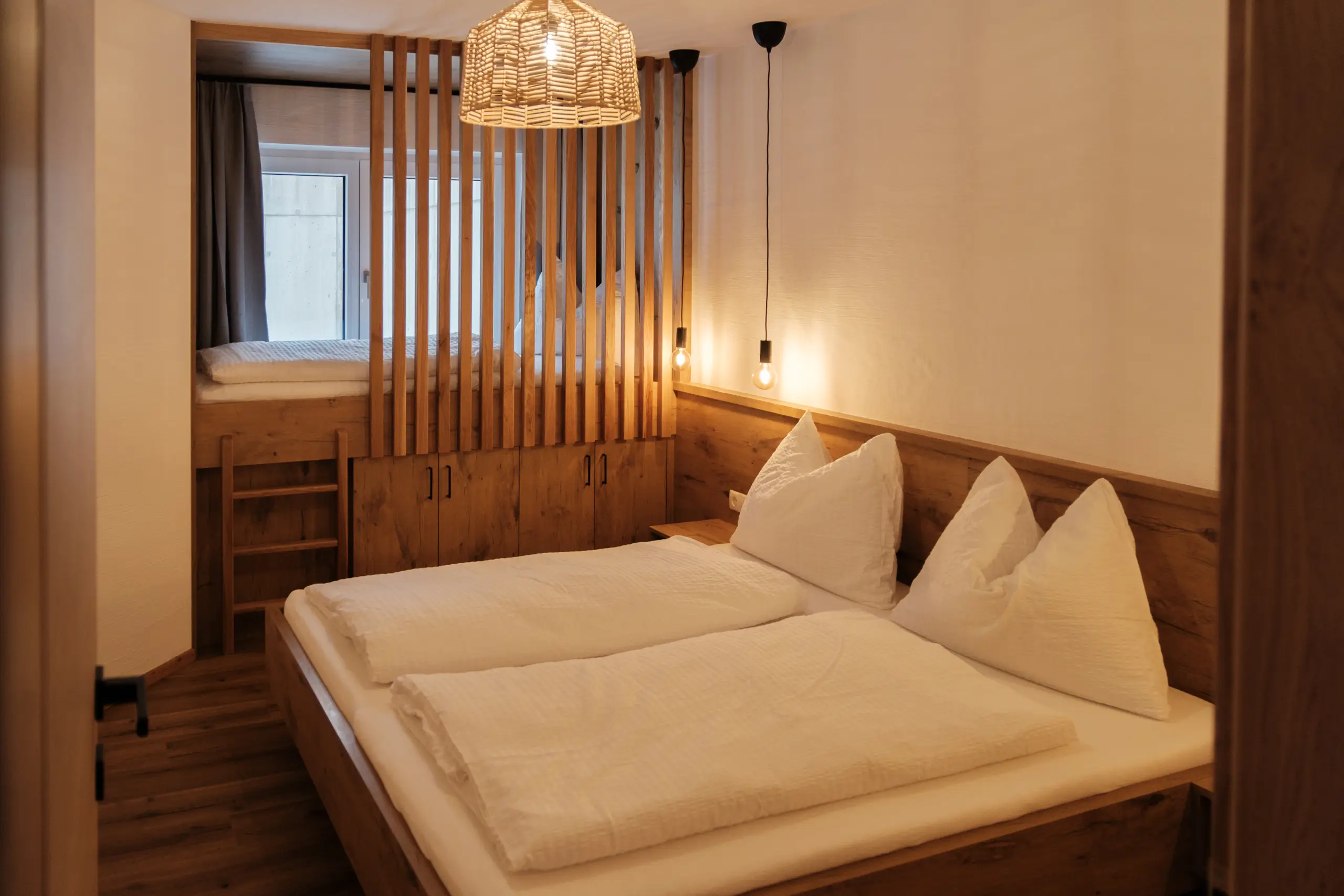 Gemütliches Schlafzimmer mit Holzbett und Hochbett, getrennt durch Holzlamellen.