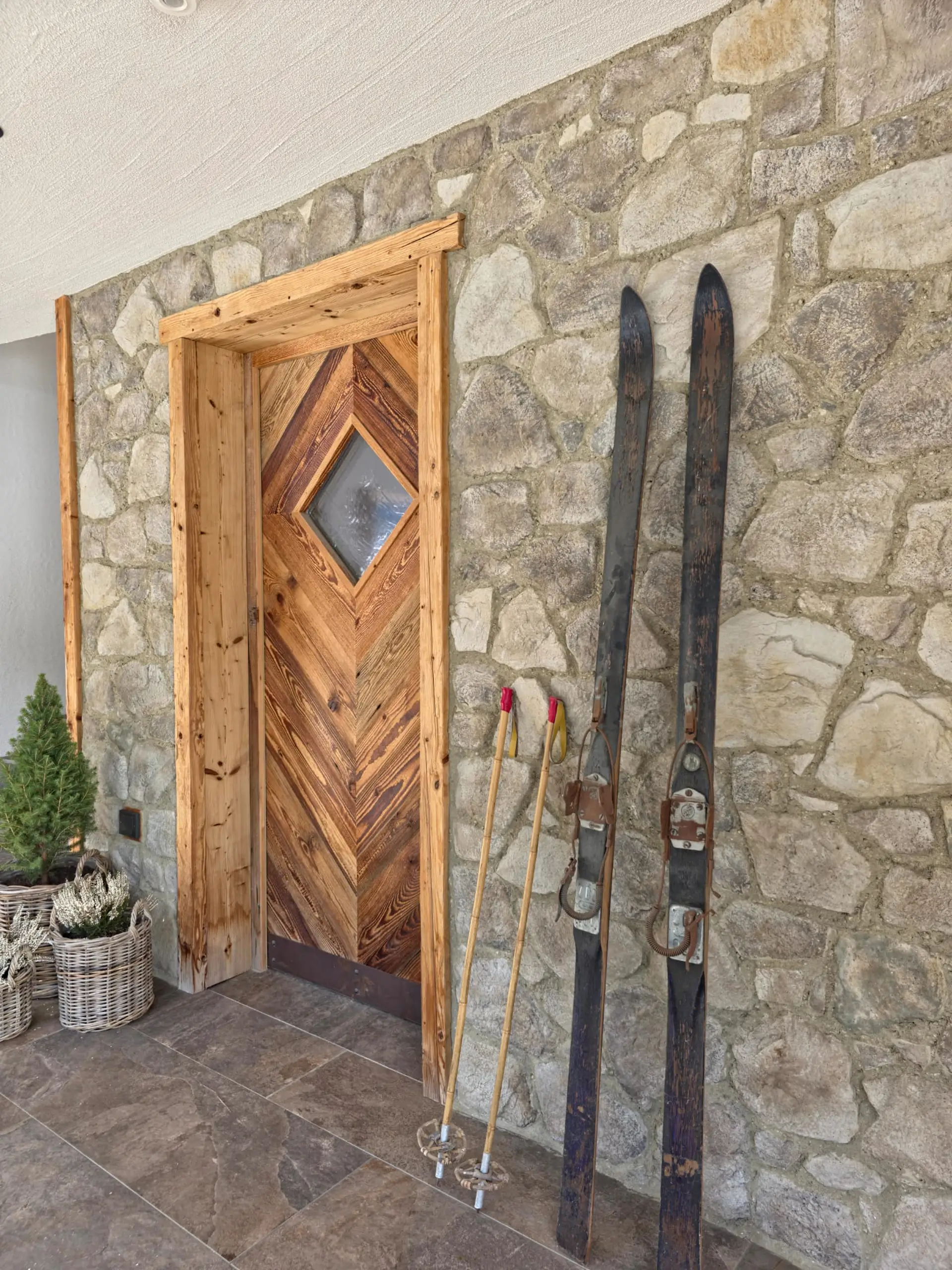 Rustikale Holztür mit Steinfassade und alten Skiern. Gemütliches Alpenambiente.