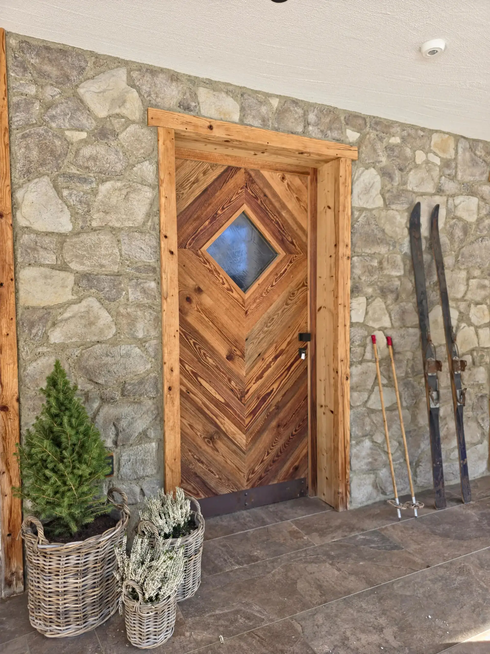 Rustikale Holztür mit Steinmauer, Ski und Pflanzenkörben.