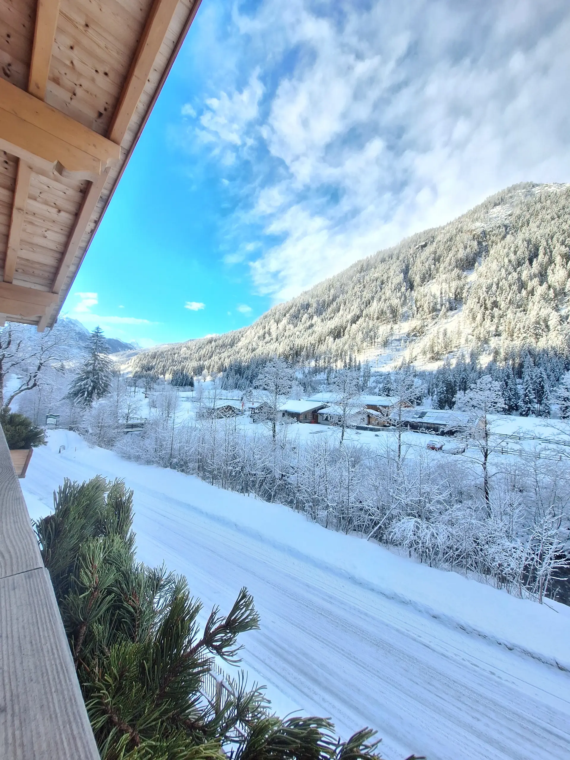 Winterlandschaft mit schneebedeckten Bergen und Häusern, aufgenommen von einem Balkon aus.